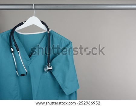 Closeup of a doctor\'s scrubs and stethoscope on hanger against a neutral background. Green surgical smock on a white hanger with a gray background with copy space.