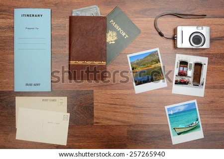 High angle shot of a passport, wallet, post cards, camera, pictures, and itinerary folder on a wood desk. Horizontal format with copy space in the middle. Photos could easily replaced with yours.