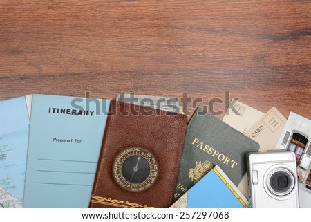 High angle shot of a travel still life. Items include: passport, wallet, post cards, camera, pictures, maps, and itinerary folder on a wood desk. Horizontal format with copy space at the top.