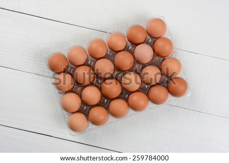 High angle shot of a 24 pack of organic brown eggs on a rustic white wood table. Horizontal format with copy space.