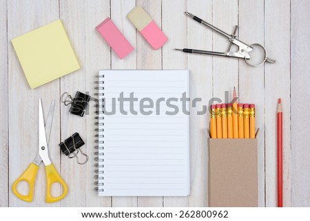 A group of items typically found in a school desk. Items include: erasers, pencils, compass, scissors, paper, note pad, paper clips, shot from a high angle.
