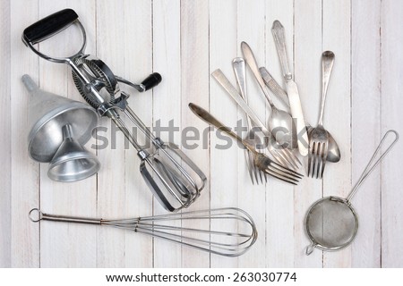 Overhead shot of a group of old kitchen utensils on a rustic wood kitchen table.