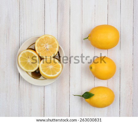 High angle still life of three whole lemons and three lemon halves in a bowl on a rustic white wood kitchen table.