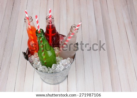 A bucket of soda bottles shot from a high angle on a rustic wood picnic table. Horizontal format with copy space. Four different open drinks with straws in the bottles.