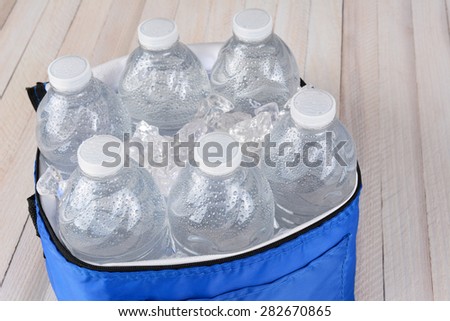 Closeup of six plastic water bottles and ice in a collapsible cooler on a white wood table. Horizontal format with copy space