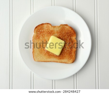 Overhead shot of a piece of buttered toast. A pat of melting butter is in the middle of the toasted white bread on a white plate