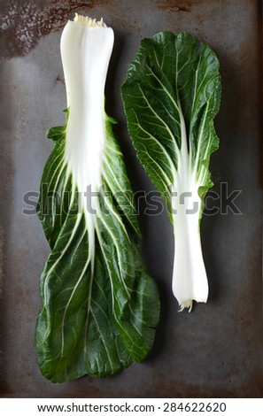 Two bok choy leaves on a used metal baking sheet. Vertical format still life..