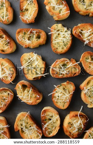 Closeup of a pan full of toasted garlic bread. The bread slices have parmesan cheese and other herbs and spices sprinkled on top. Vertical format shot from a high angle.