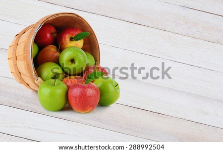 High angle shot of a basket full of Gala and Granny Smith apples spilling out onto a rustic wood surface.