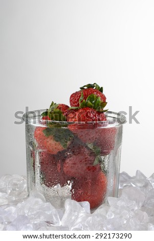 An old fashioned jar with fresh picked strawberries surrounded by crushed ice. Vertical format on a light to dark background with copy space.