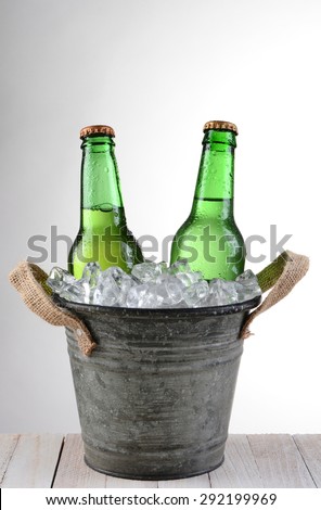 An old fashioned bucket with two beer bottles. Vertical format on a light to dark gray background with copy space.