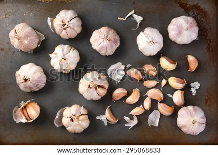 High angle view of garlic bulbs and cloves on a metal baking sheet. Whole bulbs and cloves are spread out on the surface. Horizontal format.