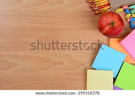 High angle back to school still life on top of a wood teachers desk. An apple, note pads, pencils and erasers with copy space.