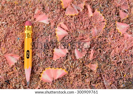 Overhead closeup of a sharpened pencil stub on a background of shavings. The well used #2 pencil is set ot the left side of the frame.