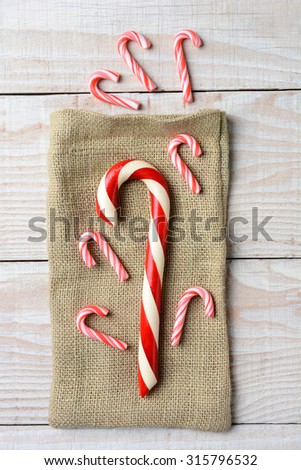 Overhead view of different sized Candy canes on a burlap bag and three on wood surface. On a rustic wood table in vertical format