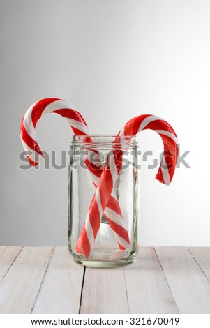 Two Candy Canes in a mason jar. The jar is on a rustic white wood table with a light to dark gray background.