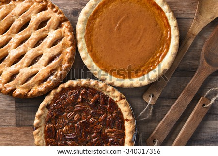 Overhead view of three pies for a Thanksgiving Holiday feast. Pecan, Apple and Pumpkin in horizontal format on wood table
