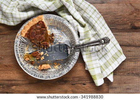 The last slice of a Thanksgiving holiday pecan pie. A tin with spatula on a wood table with kitchen towel.