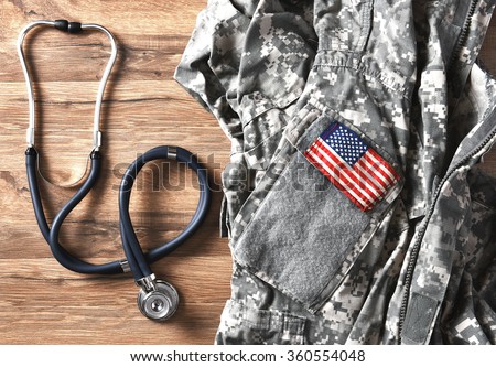 US military fatigues and stethoscope on a wood table. Military Healthcare concept.