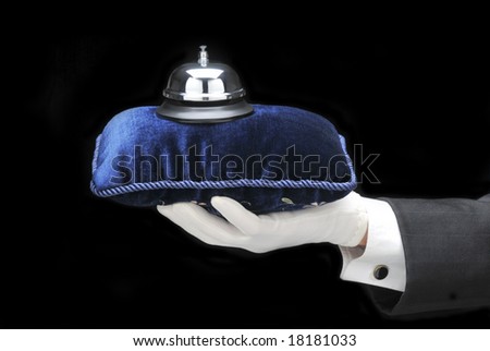 Butlers outstretched hand and arm with service bell on velvet pillow