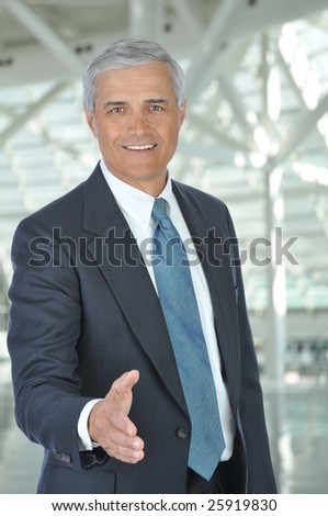 Middle Aged Businessman with hand extended to shake hands in Building Lobby