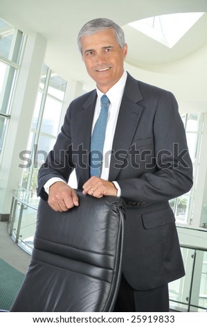 Middle Aged Businessman Standing behind His Chair in Modern Office Setting