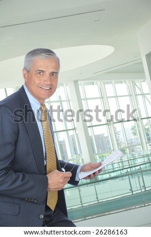 Smiling Middle Aged Businessman Holding Glasses and Newspaper seated in office setting