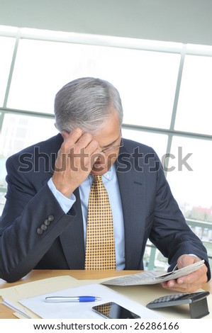 Middle Aged Businessman Seated at His Desk in Modern Office Setting Reading Newspaper