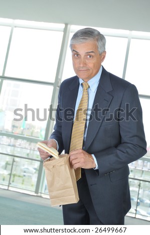 Middle Aged Businessman in office building holding brown bag and sandwich