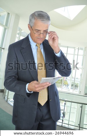 Middle Aged Businessman Standing in Modern Office Setting Reading Newspaper