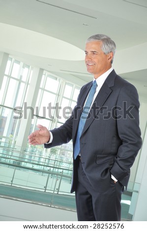 Standing Middle Aged Businessman with hand extended to shake in Office Setting