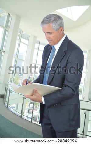 Standing mature Businessman Writing in File Folder in Office Setting