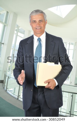 Middle Aged Businessman with file folder and hand extended to shake in office setting