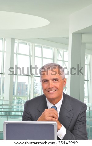 Smiling mature  Businessman Looking over top of Laptop Computer in office setting - hands clasped