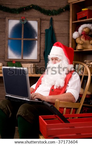 Santa Claus Sitting in Rocking Chair in Workshop Using Laptop. Vertical composition.