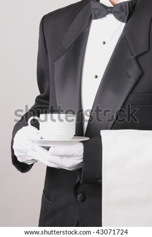 Waiter in Tuxedo holding a coffee cup with a towel draped over his arm torso only vertical format over gray background. Man is unrecognizable.