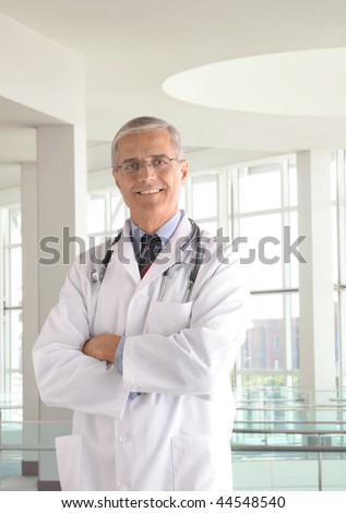 Middle aged doctor wearing lab coat and with arms crossed in modern medical facility