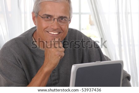 Middle aged man in front of living room window with his laptop computer.
