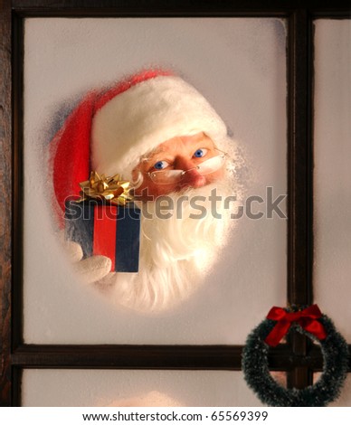 Santa Claus seen through a frosted window holding up a wrapped present.