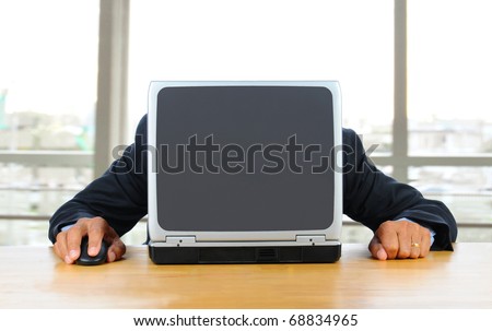 Businessman frustrated with technology with his head down on his laptop. Man is hidden behind computer only his hands and arms are visible. Horizontal format in modern office in front of window.