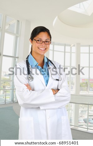 Young female medical professional wearing a lab coat in modern medical facility. Person is standing with her arms crossed and smiling