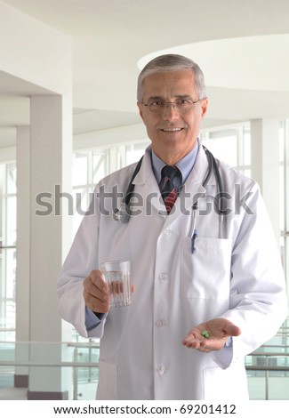 Middle aged Doctor in Labcoat with Pills and Glass of Water in modern medical facility. Vertical format.