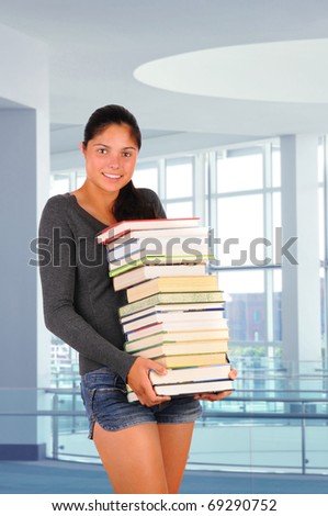 Female student carrying a stack of books in modern educational facility. Vertical format. Back to school concept.