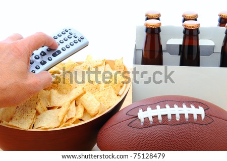 Closeup of a man\'s hand holding a TV remote with a bowl of chips six pack of beer and football isolated on white. Horizontal Format. Great for Bowl Game projects.