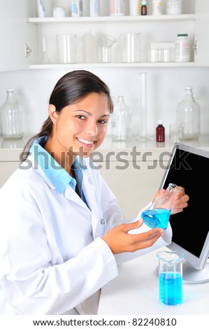 Young female Lab Tech holding up a flask of blue chemicals in laboratory setting. Vertical format.