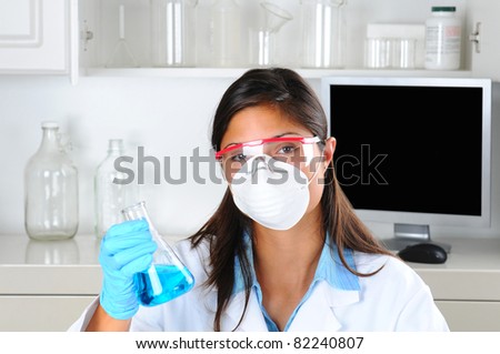 Young female Lab Tech holding up a flask of blue chemicals in laboratory setting. Horizontal format.