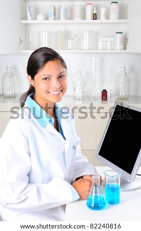 Young female Lab Tech in laboratory setting with beakers of chemicals and computer monitor. Vertical format.