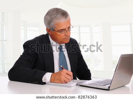 Smiling Middle Aged Businessman at desk using laptop computer with concerned expression. Horizontal format in modern office setting