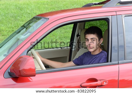 A confident newly licensed teenage male driver sits in his shiny new red car. Close up in horizontal format showing the young caucasian man as he sits behind the wheel.