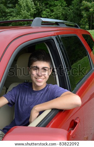 A newly licensed teenage male driver sits in his shiny new red car. Close up in vertical format showing the young caucasian man smiling as he sits behind the wheel.